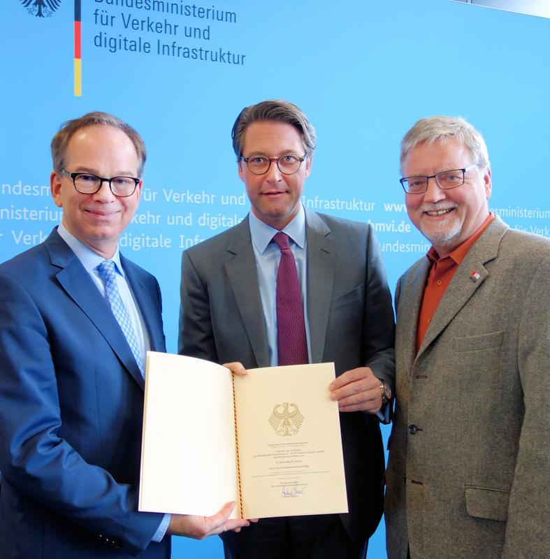 Professor Schotten (li.) erhält den Förderbescheid von Bundesverkehrsminister Andreas Scheuer (Mitte) im Beisein des Bundestagsabgeordneten Gustav Herzog. 