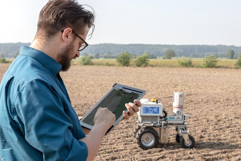 Ein Wissenschaftler des DFKI-Labors Niedersachsen gibt dem Robotersystem AROX den Weg über ein Feld vor.