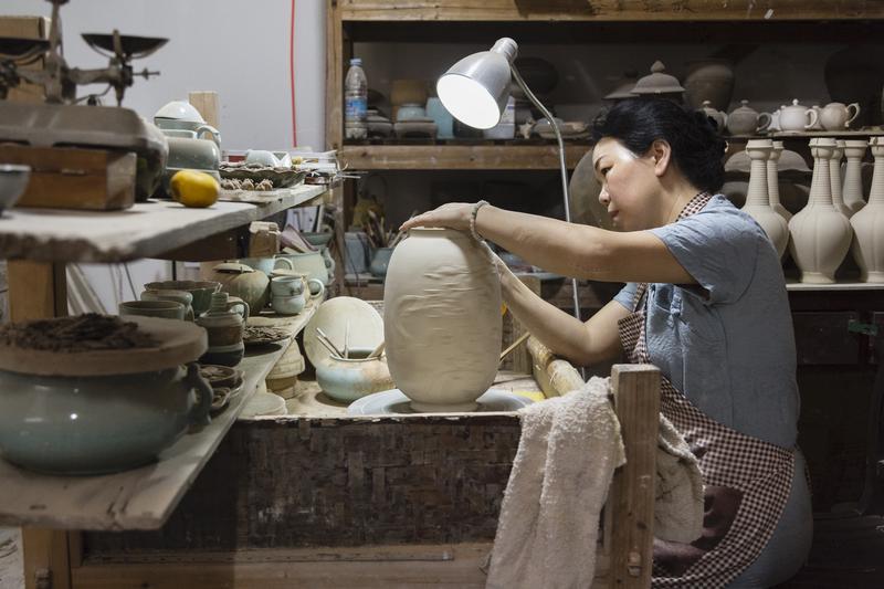 Meisterin Chen Shaoqing in ihrer Werkstatt beim Signieren einer Vase.