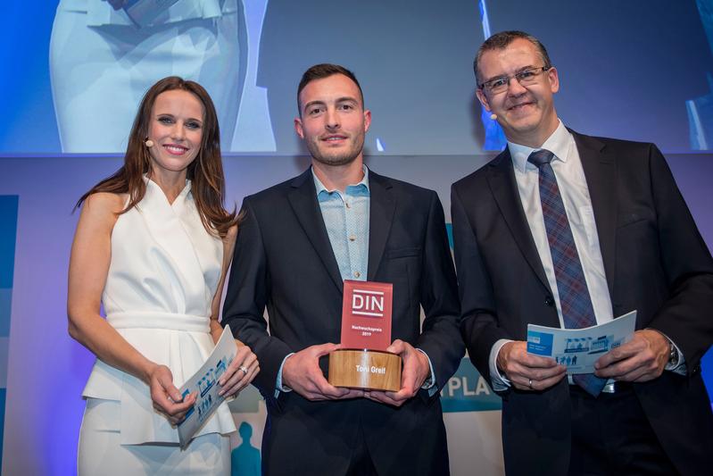 Toni Greif (M.) bei der Preisverleihung in Berlin mit dem DIN-Vorstandsvorsitzenden Christoph Winterhalter und Moderatorin Susanne Schöne. 