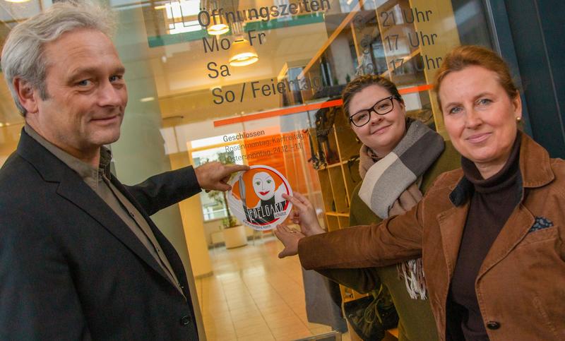 Dietrich Rebholz-Schuhmann (Wiss. Direktor), Deborah Danowski (Gleichstellungsbeauftragte) und Gabriele Herrmann-Krotz (Kfm.-Adm. Geschäftsführerin) bringen das EDELGARD-Emblem an.