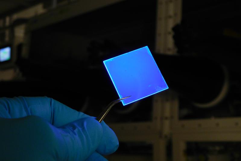 Eine mit mehreren Lagen extrem dünner Halbleiter-Nanoplättchen beschichtete Glasscheibe, die mit UV-Licht beschienen wird und blaues Licht aussendet. 