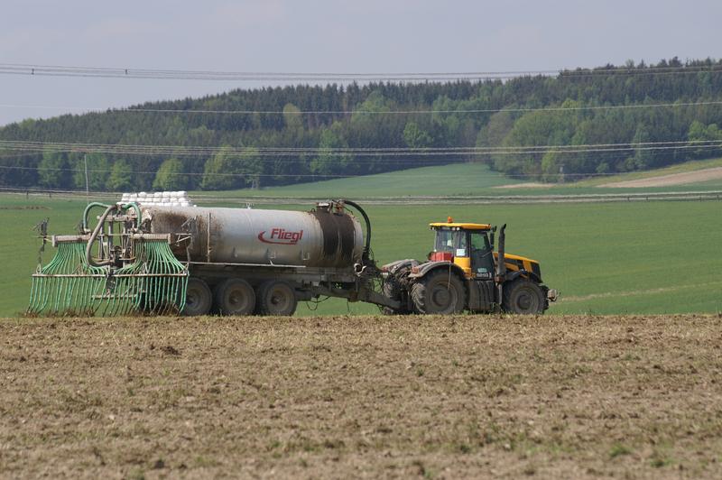 Ein Trecker bringt Gärrest auf einer landwirtschaftlichen Ackerfläche aus Gärrestausbringung auf einer landwirtschaftlichen Ackerfläche