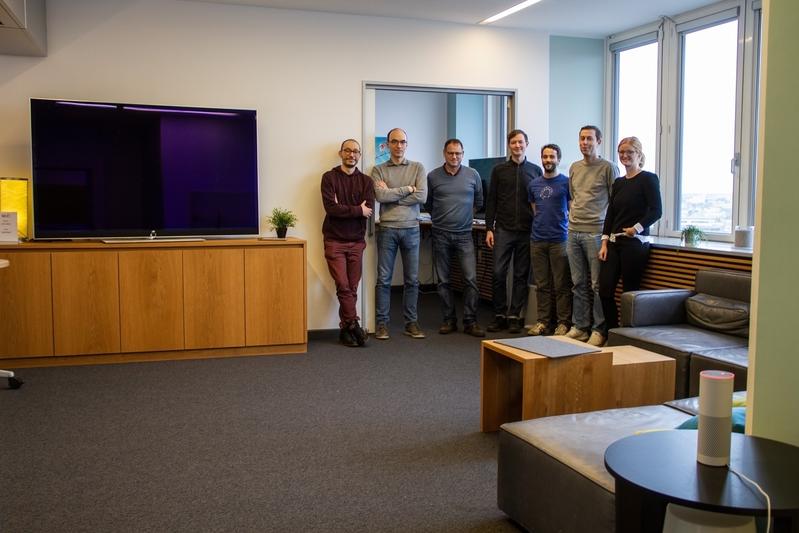 The involved scientists of the DFKI and the TU Berlin stand together in the Living Lab of the DAI Laboratory in the Telefunken building of the TU Berlin.