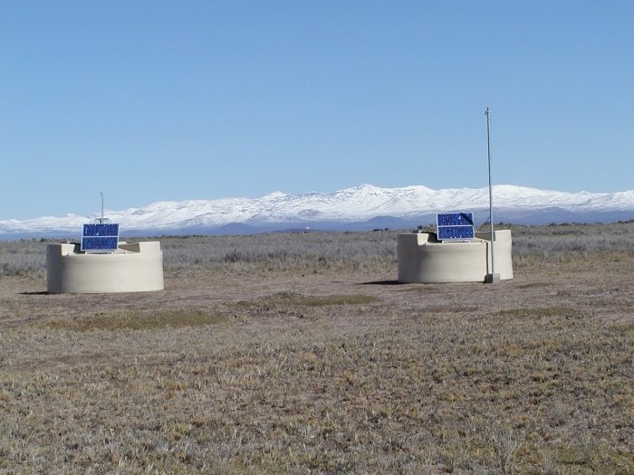 Wassertanks zum Nachweis der Cherenkov-Strahlung durch die Teilchenschauer. Zwischen den Wassertanks ist im Hintergrund vor der Kulisse der Anden das Teleskopgebäude auf Los Leones in ca. 5 km Entfernung zu erahnen.