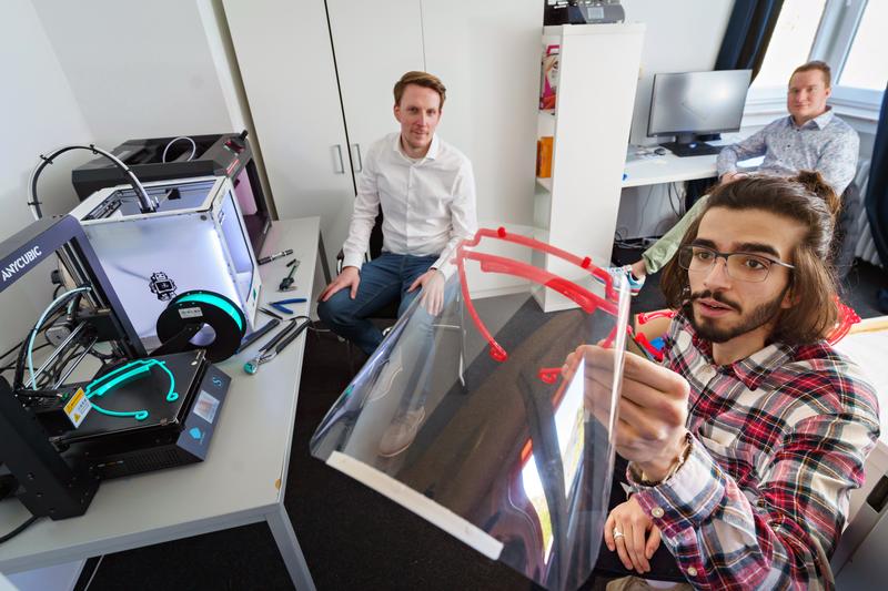 Marcel Witting, wissenschaftlicher Mitarbeiter (links), und die beiden studentischen Hilfskräfte Eyad Mustafa (vorne) und Julian Kleinkröger (hinten) haben ein Auge auf die 3D-Drucker.
