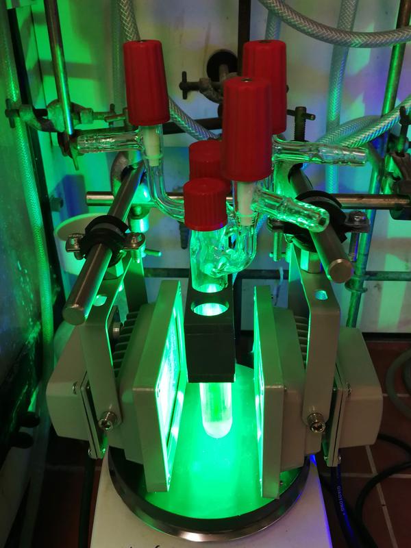 Kolben mit dem Titan-Katalysator und dem roten Farbstoff, die im Labor des Kekulé-Instituts für Organische Chemie und Biochemie der Universität Bonn mit grünem Licht bestrahlt werden. 