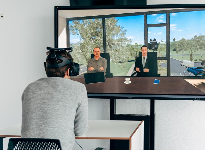 Ein Nutzer testet das Verhandlungstraining per VR-Brille. Seine virtuellen Verhandlungspartner sitzen ihm gegenüber. 