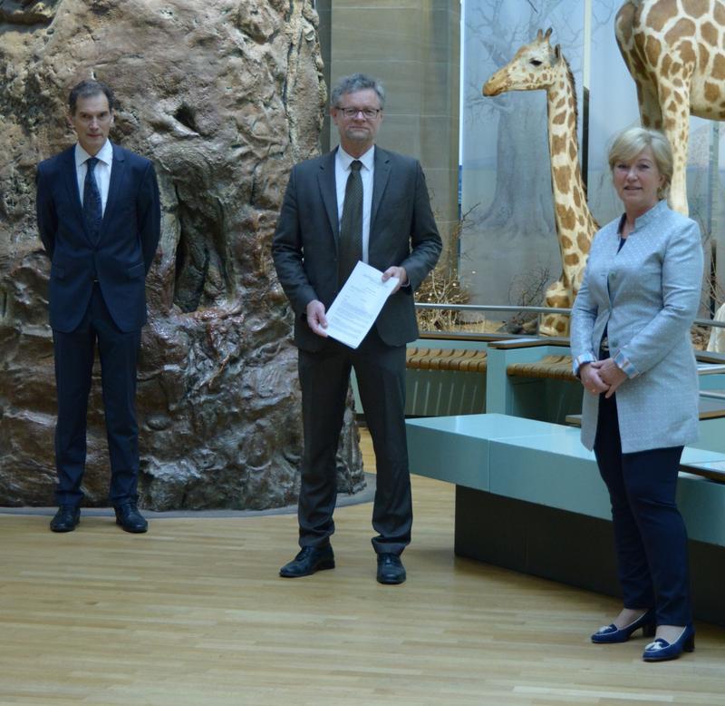 Dr. Michael Wappelhorst, Prof. Dr. Bernhard Misof, Staatsekretärin Annette Storsberg (vlnr) mit dem gerade unterzeichneten Vertrag im Ausstellungsteil „Savanne“ des Museums Koenig