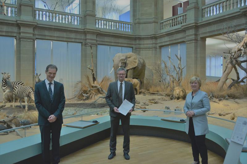 Dr. Michael Wappelhorst, Prof. Dr. Bernhard Misof, Staatsekretärin Annette Storsberg (vlnr) mit dem gerade unterzeichneten Vertrag im Ausstellungsteil „Savanne“ des Museums Koenig