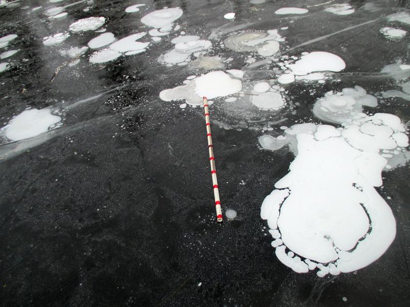 Unter dem See-Eis formen sich Methanblasen, die per Satellit erfasst werden können. Ein Zollstock (in Metern) liegt als Größenvergleich auf dem Eis. 