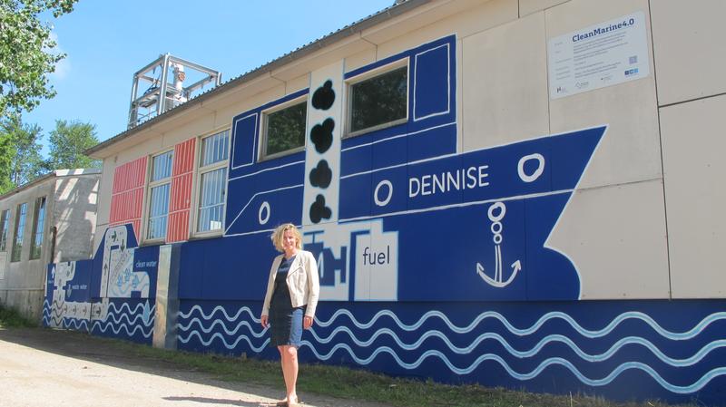 Prof. Dr. Wiktoria Vith vor einem Graffiti, das den Versuchsaufbau in der Halle in Kielseng zeigt. So bekommt die Öffentlichkeit einen Eindruck, was an der Hochschule Flensburg passiert. 