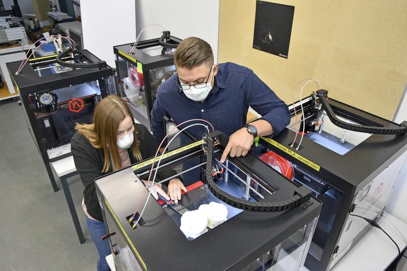Maike Krämer und Maximilian Köthe entnehmen die Masken aus dem 3D-Drucker.
