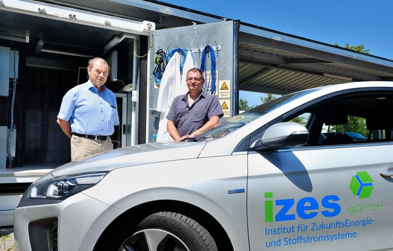 Prof. Dr. Rolf Hempelmann (l.) und Dr. Bodo Groß, Leiter des Arbeitsfelds "Technische Innovationen" des Instituts für ZukunftsEnergie- und Stoffstromsysteme IZES in Saarbrücken. Im Hintergrund die Versuchsanlage der Wissenschaftler. 