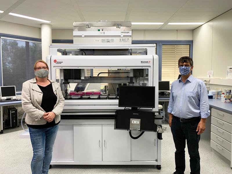 Prof. Dr. Gérard Krause (HZI) und Dr. Nicole Schneiderhan-Marra (NMI) vor dem Pipettierroboter, der zur Analyse der Blutproben mit hohem Durchsatz eingesetzt wird.  