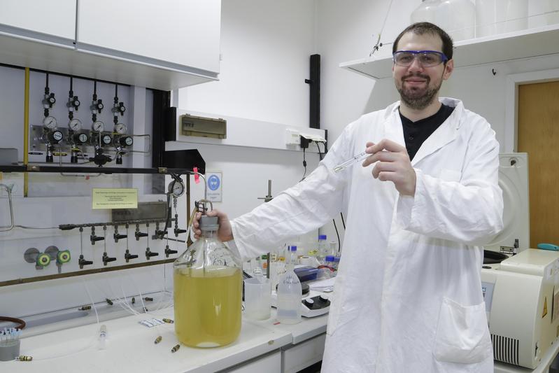Doktorand Dragan Trifunovic mit einer großen Flasche und einem kleinen Reagenzglas, die kultivierte Thermotoga maritima-Bakterien enthalten. (Foto: Uwe Dettmar für Goethe-Universität Frankfurt)