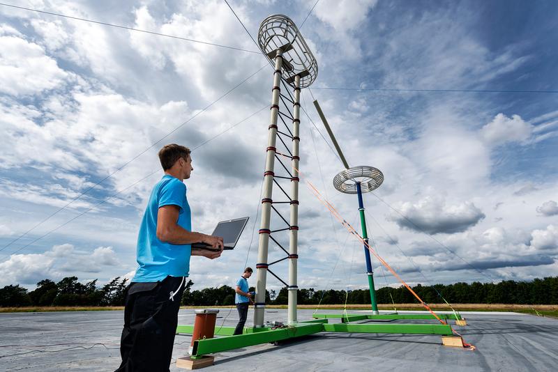 Die Messeinrichtung auf dem Freifeld der PTB besteht aus einem Hochspannungserzeuger (im Vordergrund), der Gleich-spannungen von bis zu 2 Millionen Volt erzeugen kann. Im Hintergrund steht der Messteiler, welcher diese Spannung präzise misst. 