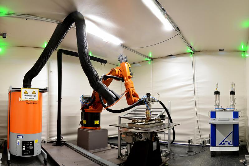 Der Industrieroboter mit Bearbeitungskopf in der Laserschutzeinhausung 