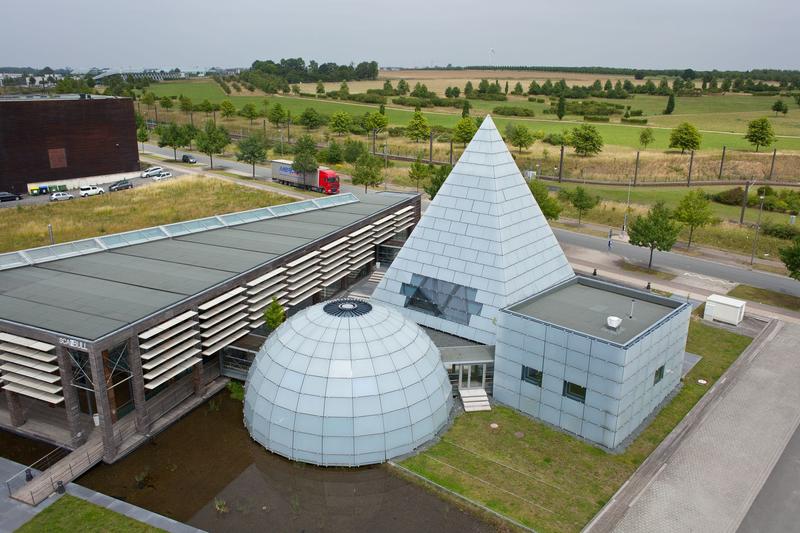 Als Reallabor dient eine Fassade des dänischen Pavillons auf dem Messegelände: Hinter dem Kubus entsteht derzeit ein weiteres würfelförmiges Gebäude, in dessen Südfassade Photovoltaik-Module integriert werden.