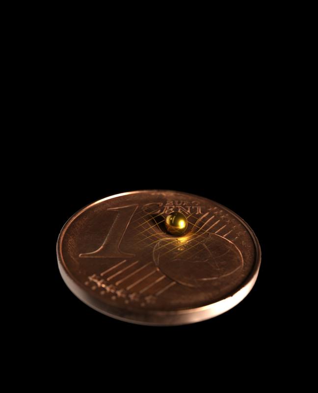 Die verwendete Goldkugel im Größenvergleich mit einer 1-Cent-Münze. Laut Einsteins Allgemeiner Relativitätstheorie krümmt jede Masse die Raumzeit 