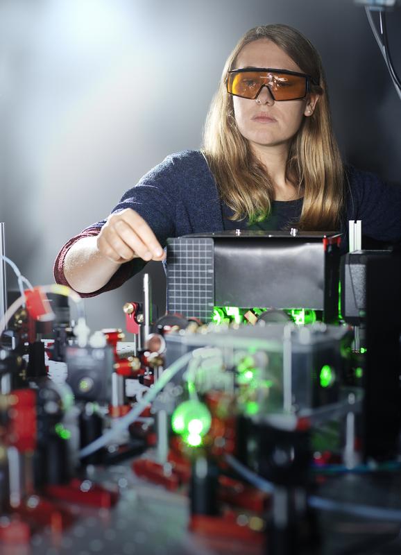 Eine Physikerin der PTB justiert den Laser auf einem optischen Tisch.