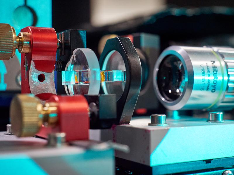 Der mit Farbstofflösung (gelb) gefüllte optische Mikroresonator. Rechts ist ein Mikroskopobjektiv zu sehen, das zur Beobachtung und Analyse des aus dem Resonator austretenden Lichts genutzt wird. 