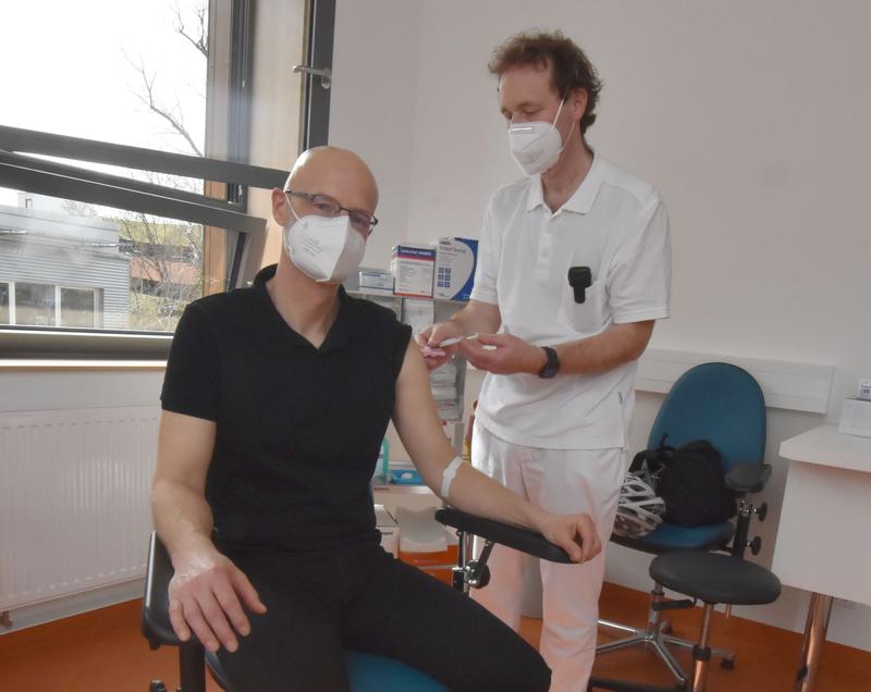 Prof. Gunnar Folprecht, Leiter des Fachbereichs Onkologie (rechts) impft Peer Schmidt. Der Leukämiepatient wird  am Dresdner Uniklinikum ambulant nachbetreut und erhielt im Rahmen einer Routineuntersuchung seine erste Impfung gegen das Corona-Virus.