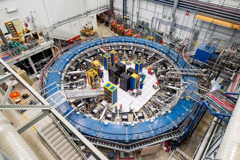 The Muon g-2 ring sits in its detector hall amidst electronics racks, the muon beamline, and other equipment.