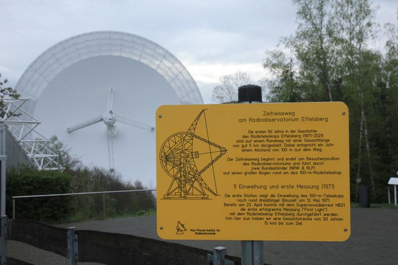 Der Zeitreiseweg am Radioteleskop Effelsberg beginnt am Besucherpavillon. Das Bild zeigt Station Nr. 1 (Einweihung und erste Messung 1971) vor dem Eingang des Pavillons und im Hintergrund das 100-m-Radioteleskop.
