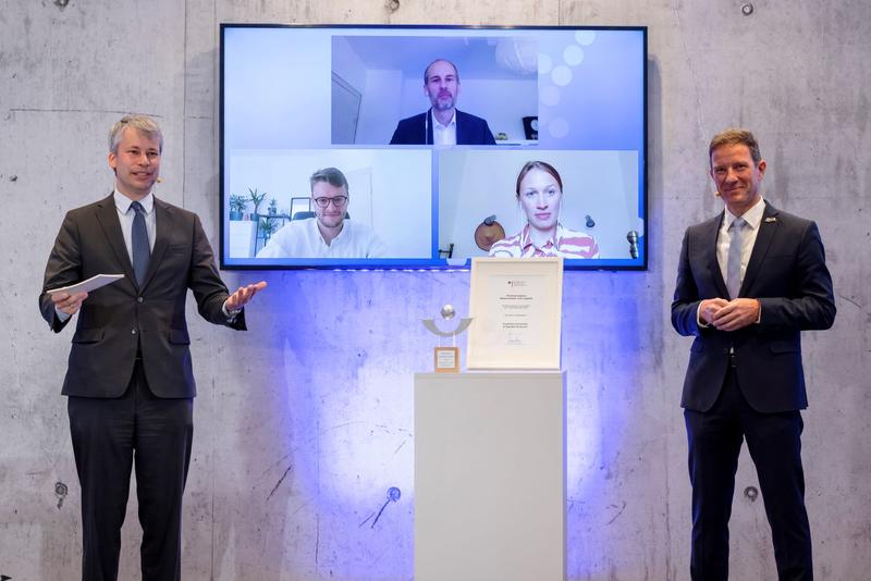 Steffen Bilger (links) gratuliert Prof. Dr. Kai-Oliver Schocke (rechts) zum Hochschulpreis. Auf dem Screen im Hintergrund: Prof. Dr. Benjamin Bierwirth (oben) sowie Studierende des Master-Studiengangs Global Logistics Benjamin Walling und Theresa Wörmann