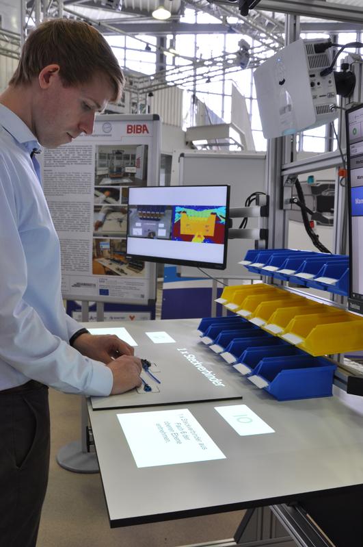 BIBA-Wissenschaftler und Projektleiter Christoph Petzoldt 2019 noch in der Anfangsphase des F&E-Vorhabens „Gamifiziertes KI-Assistenzsystem zur Unterstützung des manuellen Montageprozesses“ (AxIoM) am Projekt-Versuchsaufbau in der BIBA-Forschungshalle. 