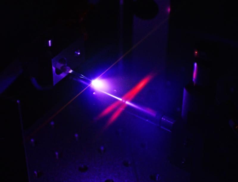 Generation of attosecond pulses in a jet of neon gas within the enhancement resonator cavity. The excitation of the gas atoms makes the intersecting infrared laser beams (shown in red) in the resonator visible to the human eye. 