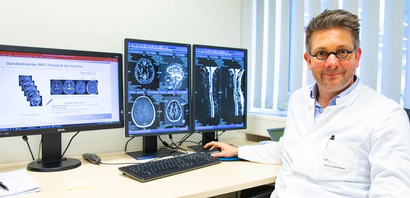 Professor Dr. Wattjes in front of two monitors with slice images of altered brain structures caused by multiple sclerosis
