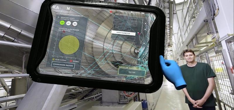 Einblick in die VR-Anwendung: Der Physiker Dr. Manuel Klein erklärt neben dem Hauptspektrometer-Tank das KATRIN-Experiment. Mit dem virtuellen Tablet können die Benutzerinnen und Benutzer der VR-Anwendung das Experiment steuern.(Quelle: Screenshot Anwend)