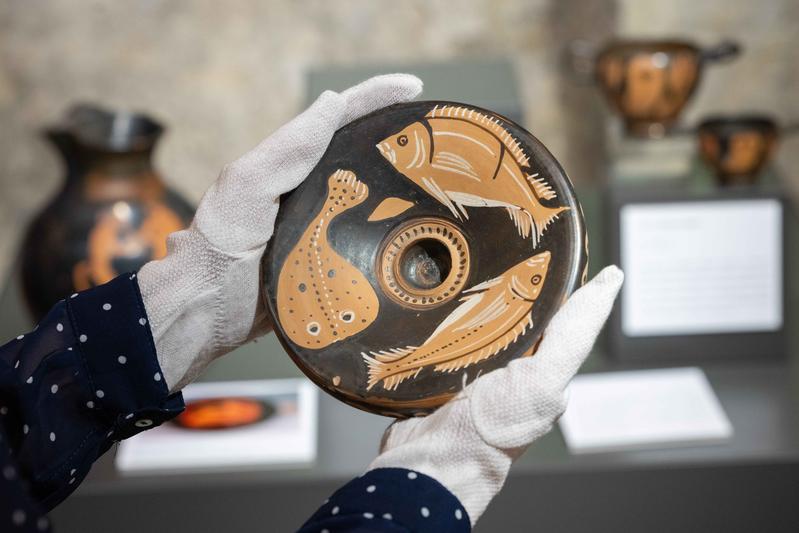 Eine Mitarbeiterin präsentiert einen Fischteller in der neuen Ausstellung „Mehr als Brot und Wein. Antike Speisen – Alltagskost und Tafelluxus" in der Universität Jena.