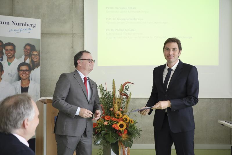 Foto: Privatdozent Dr. Francesco Pollari PhD (r.) erhält von Forschungsdekan Prof. Dr. Sascha Pahernik die Urkunde als „Forscher des Jahres“ der PMU Nürnberg.