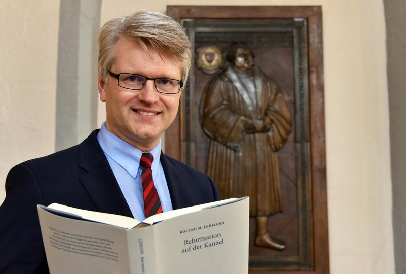 Der Kirchenhistoriker Roland M. Lehmann mit seinem neuen Buch vor der Grabplatte Luthers in Jena.