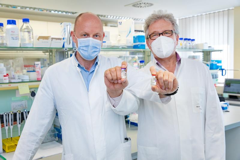  Professor Behrens und Professor Förster im MHH-Institut für Immunologie mit über Kreuz gehaltenen Impfampullen der Firmen AstraZeneca und Biontech/Pfizer. 