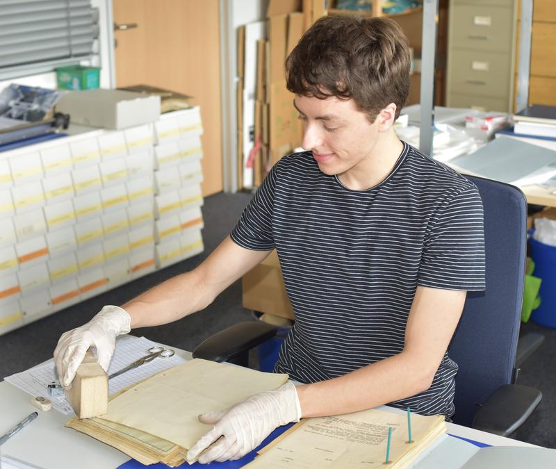 Student employee Alexander Timm cleans old documents so that they can be preserved for posterity in the archive for a long time.