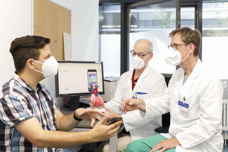 Studienteilnehmer Daniel Foydl (l.) im Gespräch mit Prof. Dr. Matthias Pauschinger (r.), dem Ärztlichen Leiter der Klinik für Innere Medizin mit dem Schwerpunkt Kardiologie, und Dr. Matthias Fittkau, Oberarzt der Klinik für Herzchirurgie