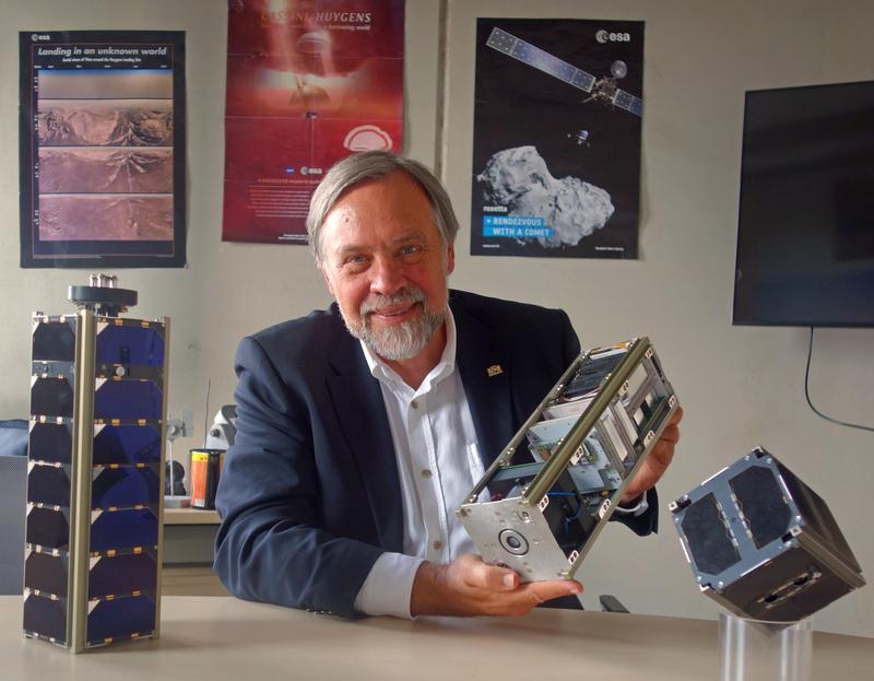 Klaus Schilling mit den Satelliten, die sein Berufsleben geprägt haben. UWE und NetSat im Vordergrund; auf den Postern im Hintergrund HUYGENS und ROSETTA, die er während seiner Tätigkeit in der Industrie mit realisieren half.
