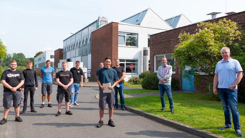 Simon Sprengel (Mitte) mit seinen Kollegen, Ausbilder Ralf Selbach (hinten rechts) und Geschäftsführer Kai de Weldige (zweiter von rechts) bei der Feier vor dem Werkstatttor am MPIE. 