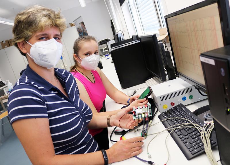 Dr. Katja Orlowski (links) und ihre studentische Hilfe Jessica Grahlmann überprüfen die Funktion des intelligenten T-Shirts mit Hilfe eines EKG-Generators, der die Aktivität des menschlichen Herzes simuliert.