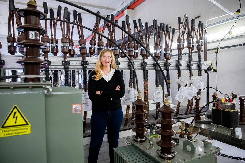 Ann-Catrin Uhr-Müller vor dem Versuchsaufbau in Köln, der Thema ihrer Doktorarbeit ist. Die Flaschen an den Kabelenden sind mit zähflüssiger Masse gefüllt: Das ist ein Öl, mit dem die Isolierschicht bei den alten Papier-Masse-Kabeln getränkt ist.