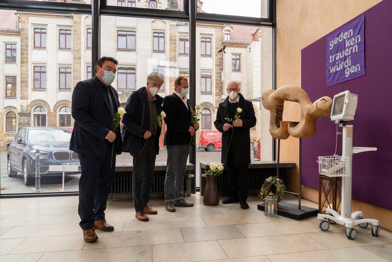 Frank Ohi, Kaufmännischer Vorstand Uniklinikum Dresden, Künstler Prof. Ulrich Eißner, Prof. Michael Albrecht, Medizinischer Vorstand Uniklinikum Dresden, und Seelsorger Pfarrer Christoph Behrens (v.l.n.r.) legen Rosen am Corona-Gedenkort nieder.