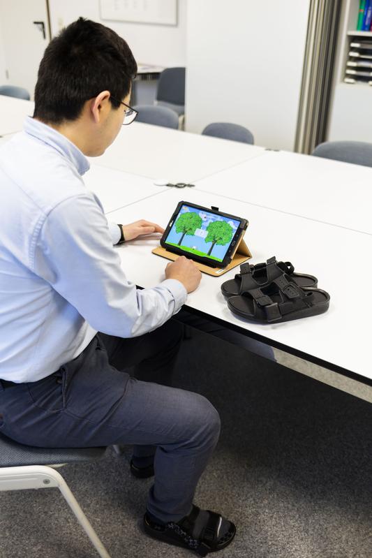 Wissenschaftlicher Mitarbeiter Antao Ming demonstriert die Funktionsweise der Schuhe mit speziellen Einlegesohlen in Verbindung mit dem Spiel auf einem Tablet.