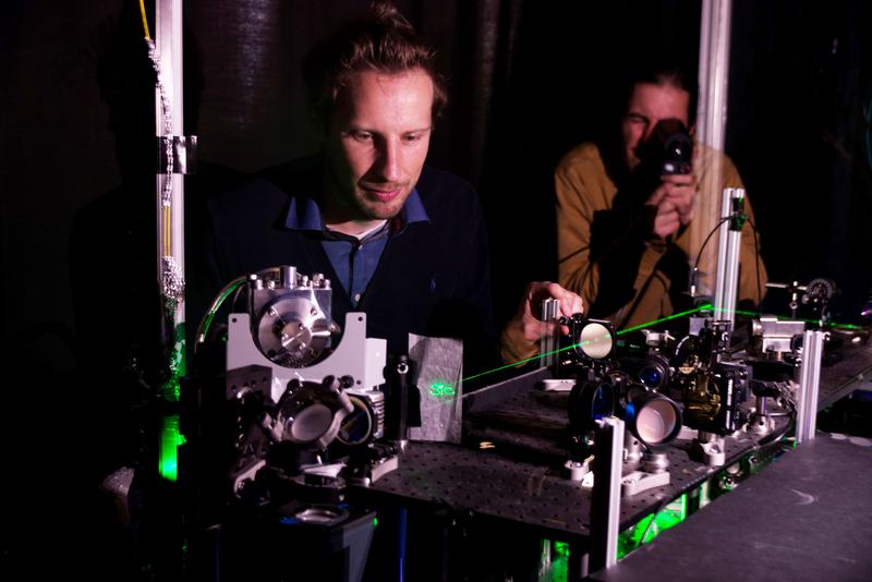 (v.l.) Dr. Florian Kaiser und Doktorand Erik Hesselmeier vor dem experimentellen Aufbau für die Publikation in Nature Materials. Die grüne Laserlinie macht den optischen Strahlpfad sichtbar gemacht.