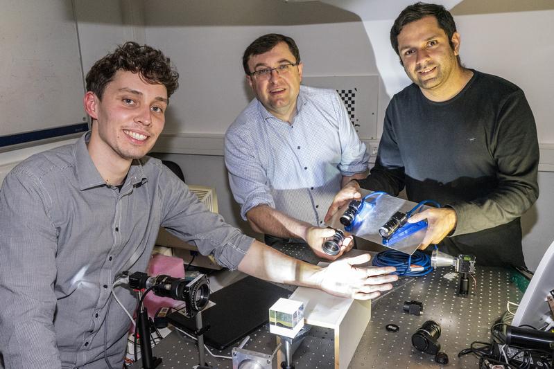 Prof. Dr. Bernhard Roth (centre) is standing at an optical table with Lennart Jütte (left) and Gaurav Sharma (right) in the HOT test lab. 