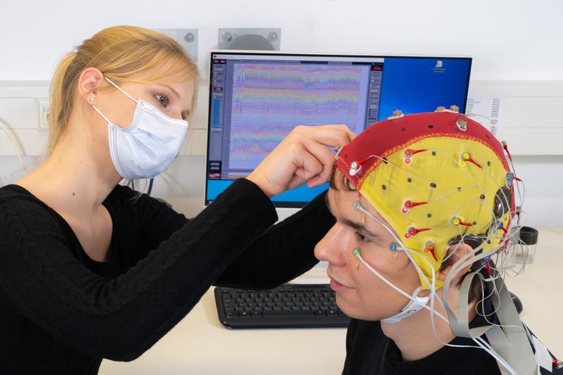 Doktorandin Celina von Eiff befestigt Elektroden an einer Kappe, die der Proband Lucas Riedel während einer EEG-Studie mit Cochlea-Implantaten an der Universität Jena trägt. 