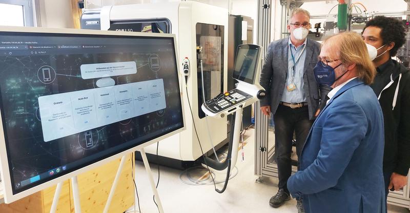 Patrick Ongom-Along, KI-Trainer der Modellfabrik Virtualisierung (ganz rechts) zeigt Dr. Holger Becker (vorn) das Dashboard der Anlagen und Demonstratoren der Arbeitsgruppe von Prof. Dr. Jens Bliedtner (hinten)